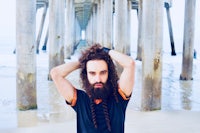 a man with long hair standing under a pier