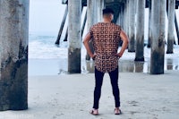 a man standing under a pier looking at the ocean