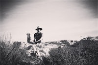 a black and white photo of a man sitting on a rock